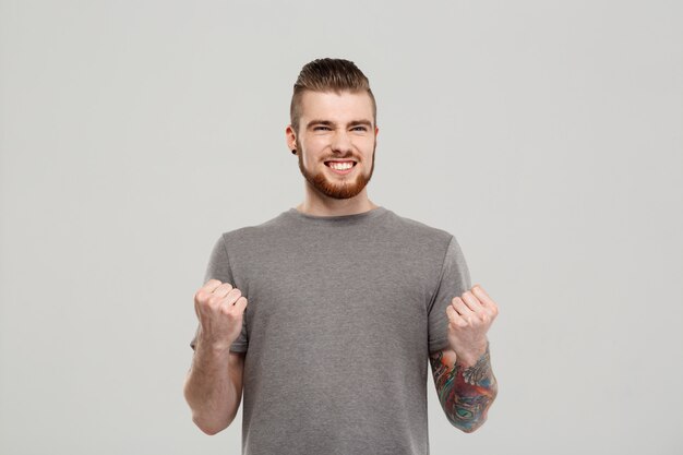 Hombre hermoso joven que disfruta sobre la pared gris.