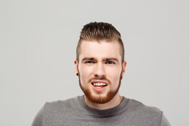 Hombre hermoso joven que gesticula sobre la pared gris.