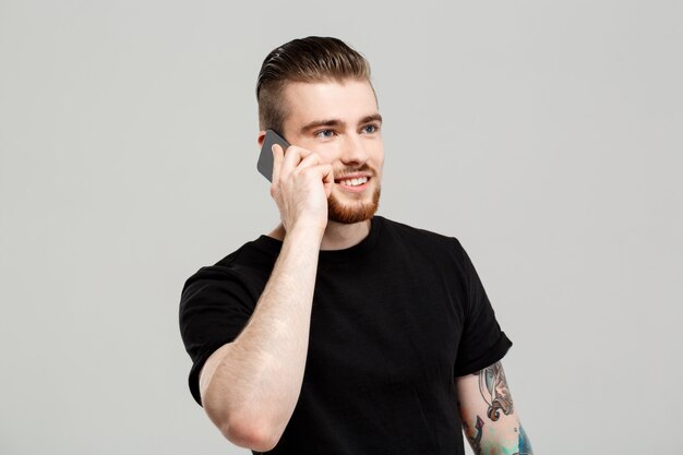 Hombre hermoso joven que habla en el teléfono sobre la pared gris.