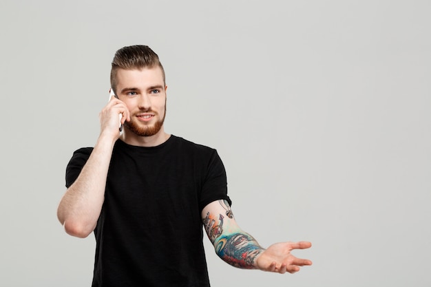 Hombre hermoso joven que habla en el teléfono sobre la pared gris.