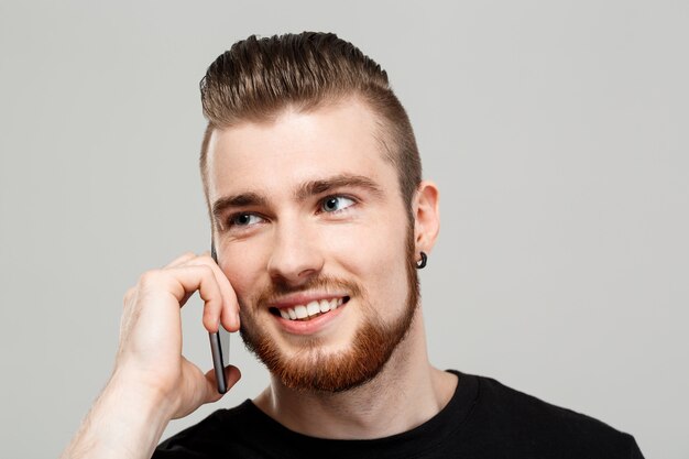 Hombre hermoso joven que habla en el teléfono sobre la pared gris.