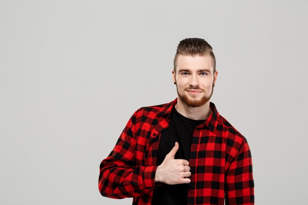 Hombre hermoso joven que muestra muy bien sobre la pared gris.