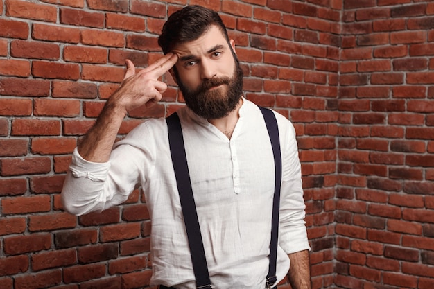 Foto gratuita hombre hermoso joven que presenta señalando los dedos el al frente en la pared de ladrillo.