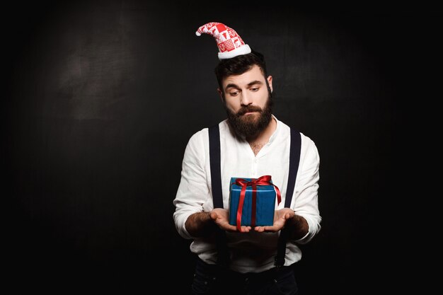 Hombre hermoso joven que sostiene la caja de regalo de la Navidad sobre negro.