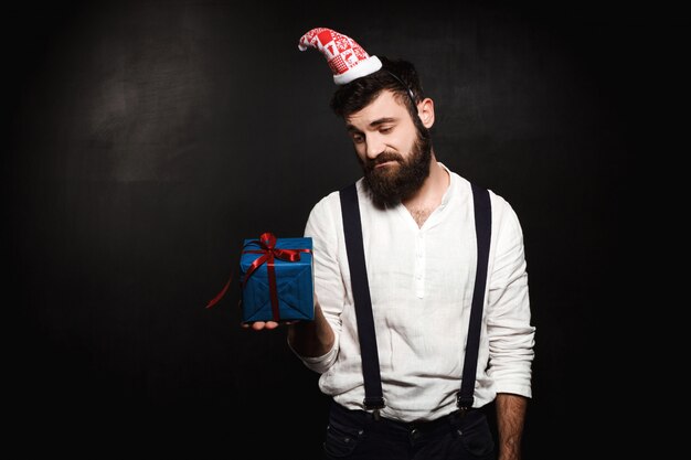 Hombre hermoso joven que sostiene la caja de regalo de la Navidad sobre negro.