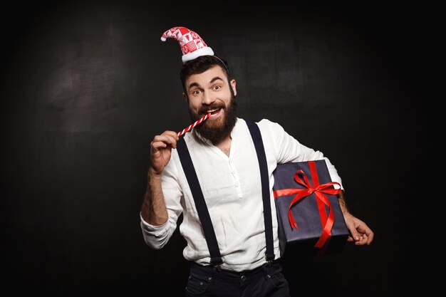 Hombre hermoso joven que sostiene la caja de regalo de la Navidad sobre negro.