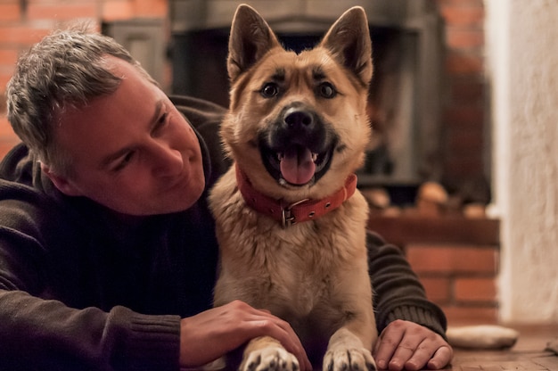 Hombre hermoso con el perro lindo en el país. Hombre atractivo que miente en suelo con su perro en el país en sala de estar. Emociones humanas positivas, expresión facial, sentimientos.