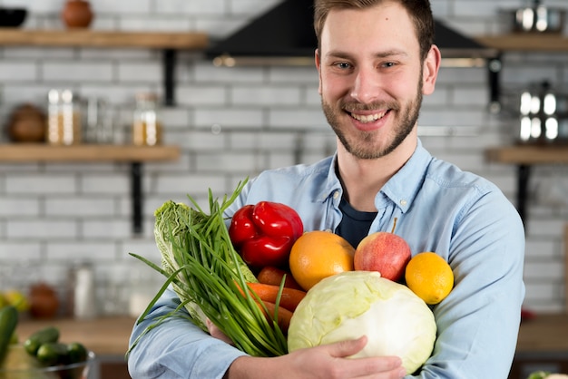 Hombre hermoso que lleva verduras crudas en cocina