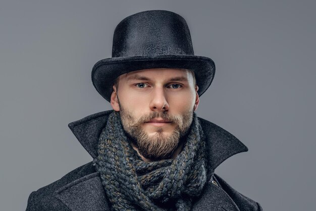 Un hombre hipster barbudo vestido con una chaqueta gris y un sombrero cilíndrico aislado en un fondo gris.