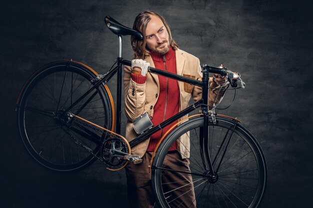 Un hombre hipster con el pelo largo y rubio sostiene una bicicleta de una sola velocidad en su hombro.