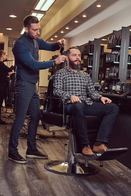 Hombre hipster en una peluquería. El peluquero profesional usa un cepillo, un peinado casi terminado.