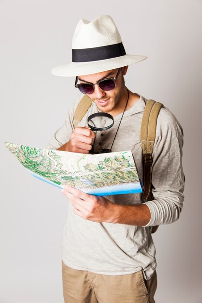 Hombre hipster usando lupa para leer mapa