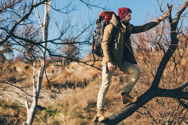 Hombre hipster viajando con mochila en el bosque de otoño con chaqueta, sombrero, turista activo, explorando la naturaleza en la estación fría