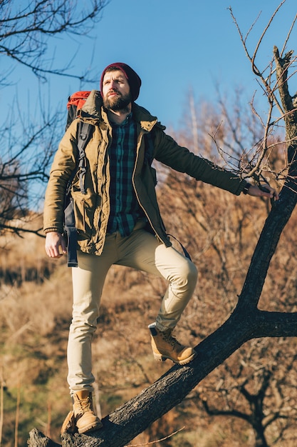Hombre hipster viajando con mochila en el bosque de otoño con chaqueta, sombrero, turista activo, explorando la naturaleza en la estación fría