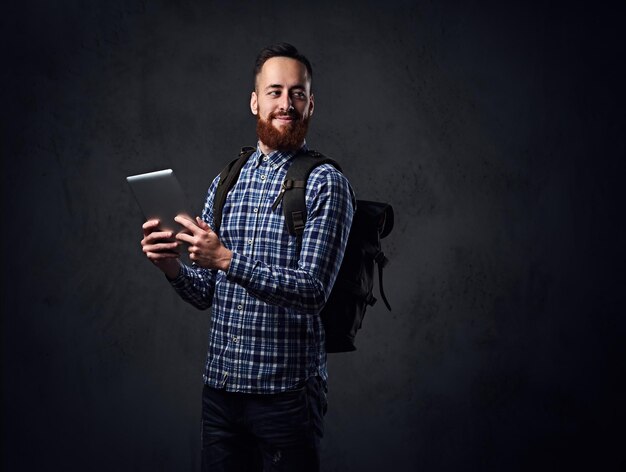 El hombre hipster viajero pelirrojo tiene una tableta y una mochila.