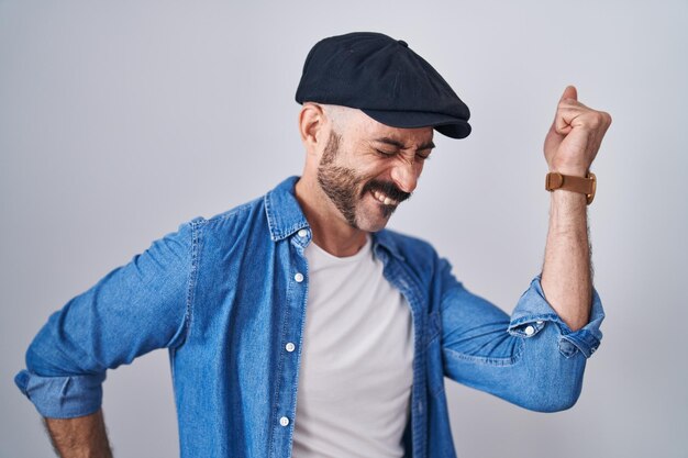 Hombre hispano con barba parado sobre un fondo aislado bailando feliz y alegre, sonriendo moviéndose casual y confiado escuchando música