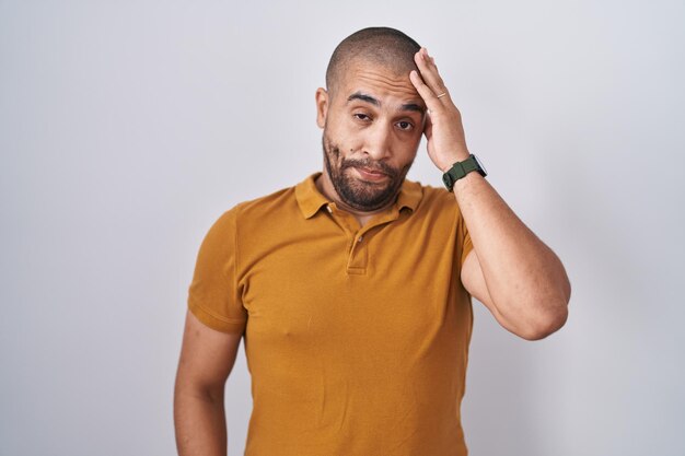 Hombre hispano con barba sobre fondo blanco preocupado y estresado por un problema con la mano en la frente, nervioso y ansioso por la crisis