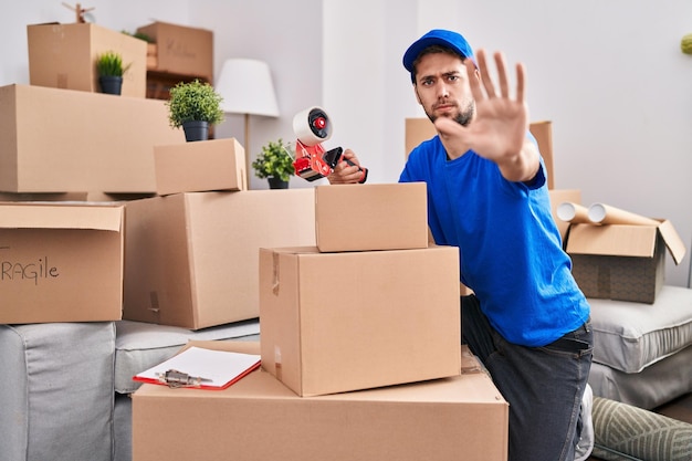 Foto gratuita hombre hispano con barba trabajando en cajas móviles con la mano abierta haciendo señas de alto con expresión seria y segura, gesto de defensa