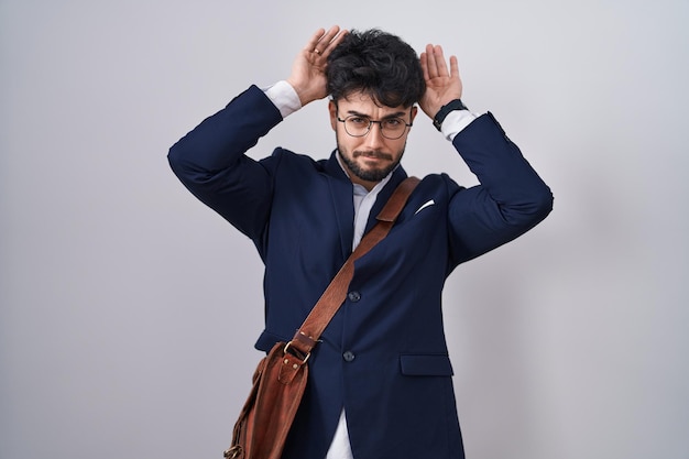 Foto gratuita hombre hispano con barba vistiendo ropa de negocios haciendo gestos de orejas de conejo con las palmas de las manos mirando cínico y escéptico concepto de conejo de pascua