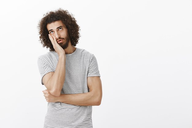 Hombre hispano guapo indiferente aburrido con barba y peinado afro, haciendo cara de palma y mirando hacia arriba con expresión cansada y harta