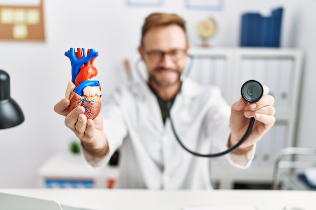 Foto gratuita hombre hispano de mediana edad con uniforme médico auscultando el corazón en la clínica