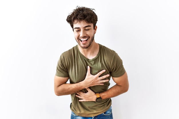 Hombre hispano de pie sobre un fondo blanco aislado sonriendo y riendo fuerte en voz alta porque es una broma divertida y loca con las manos en el cuerpo.