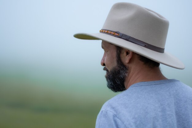 Hombre hispano con sombrero y barba de vacaciones en el campo en un brumoso