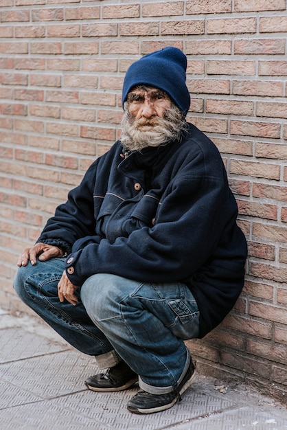 Hombre sin hogar con barba delante de la pared de ladrillo
