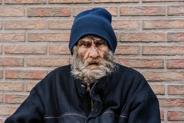 Hombre sin hogar con barba delante de la pared