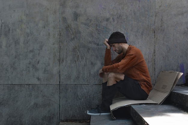 Hombre sin hogar sentado de lado sobre cartón