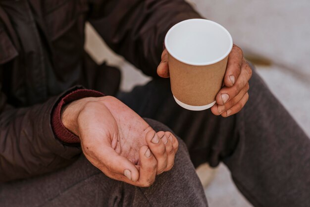 Hombre sin hogar sosteniendo la mano en busca de ayuda y taza vacía