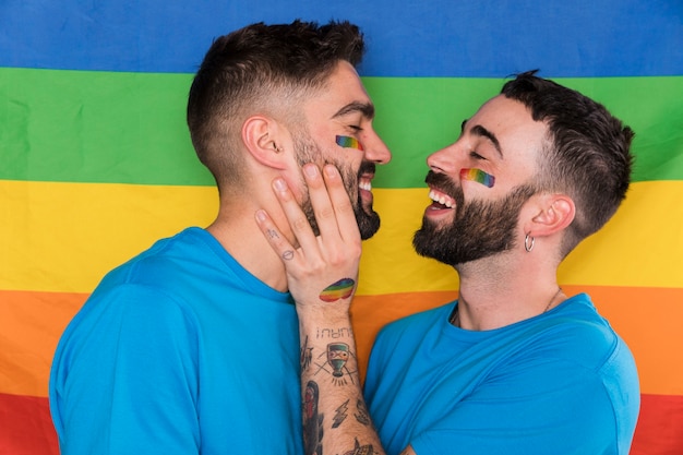 Hombre homosexual tocando la cara de los novios en una bandera multicolor LGBT