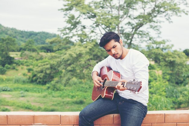 hombre inconformista joven que toca la guitarra para relajarse en sus vacaciones, enj