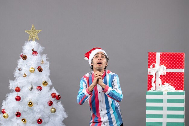 Hombre indefenso de vista frontal deseando cerca del árbol de Navidad blanco