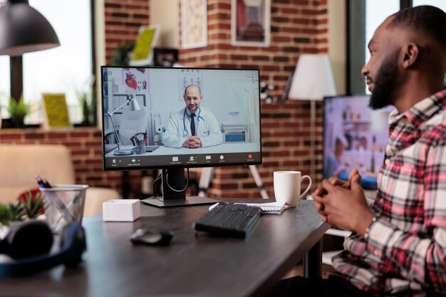 Hombre independiente charlando con un médico en una videoconferencia de telemedicina, usando una videoconferencia de telesalud en línea para hablar con un médico sobre la atención médica. Uso de computadora con cámara web de forma remota.