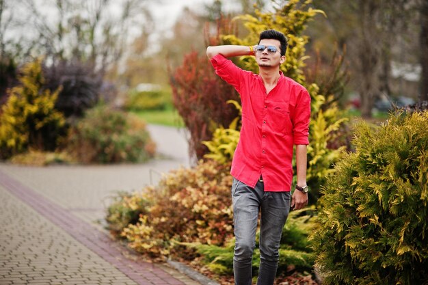 Hombre indio en camisa roja y gafas de sol posando al aire libre