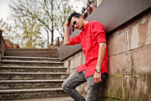 Hombre indio en camisa roja y gafas de sol posando al aire libre