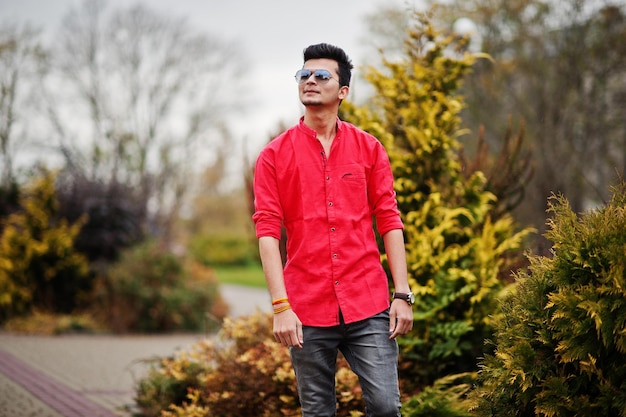 Hombre indio en camisa roja y gafas de sol posando al aire libre