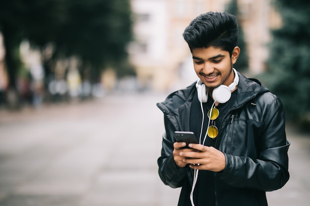 Hombre indio feliz caminando y usando un teléfono inteligente para escuchar música con auriculares