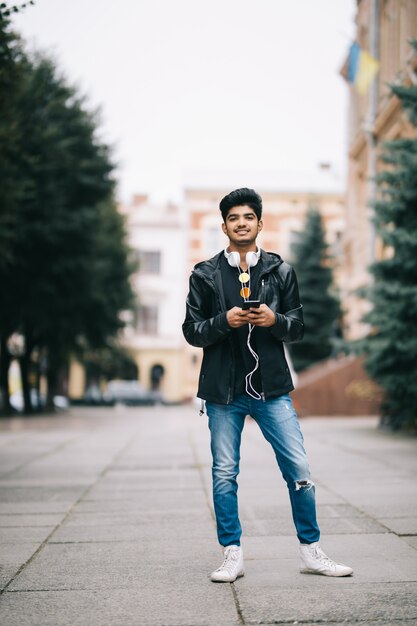 Hombre indio feliz caminando y usando un teléfono inteligente para escuchar música con auriculares