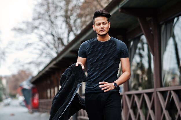 Hombre indio guapo y de moda en camisa negra con chaqueta posada al aire libre