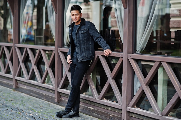 Hombre indio guapo y de moda en chaqueta de jeans negros posada al aire libre