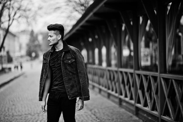 Hombre indio guapo y de moda en chaqueta de jeans negros posada al aire libre