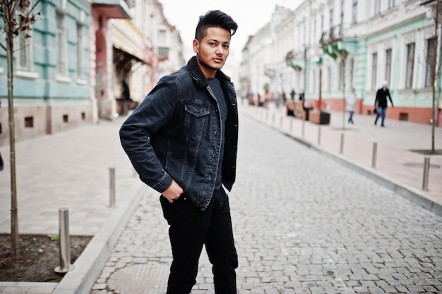 Hombre indio guapo y de moda en chaqueta de jeans negros posada al aire libre