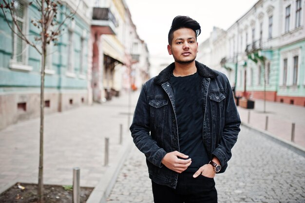 Hombre indio guapo y de moda en chaqueta de jeans negros posada al aire libre