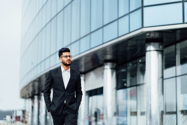 Un hombre indio moderno va a una reunión de negocios, detrás de él un edificio moderno.