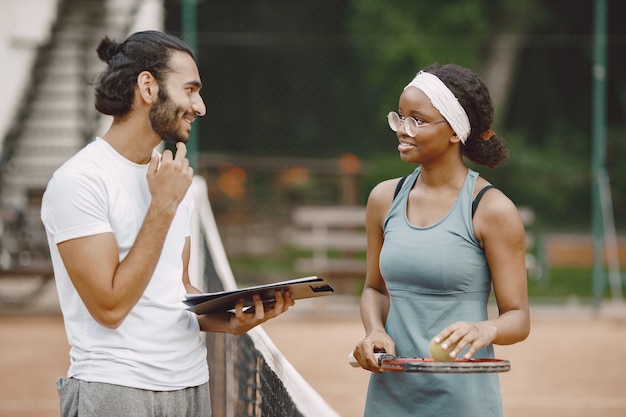 Foto gratuita hombre indio y mujer negra americana de pie en una cancha de tenis