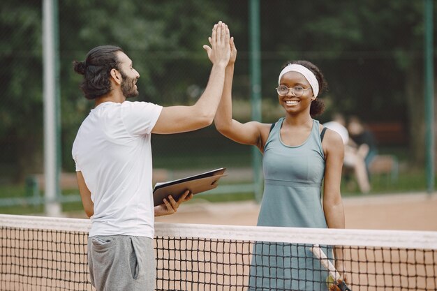 Hombre indio y mujer negra americana de pie en una cancha de tenis