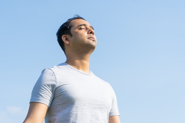 Foto gratuita hombre indio sereno meditando al aire libre con los ojos cerrados y manteniendo las manos juntas