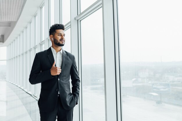 Hombre indio en traje negro junto a la ventana en un edificio moderno.